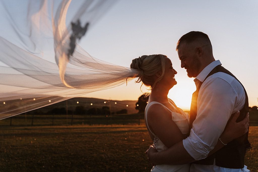 Lauryn and Tim together at sunset with a veil blowing in the breeze.