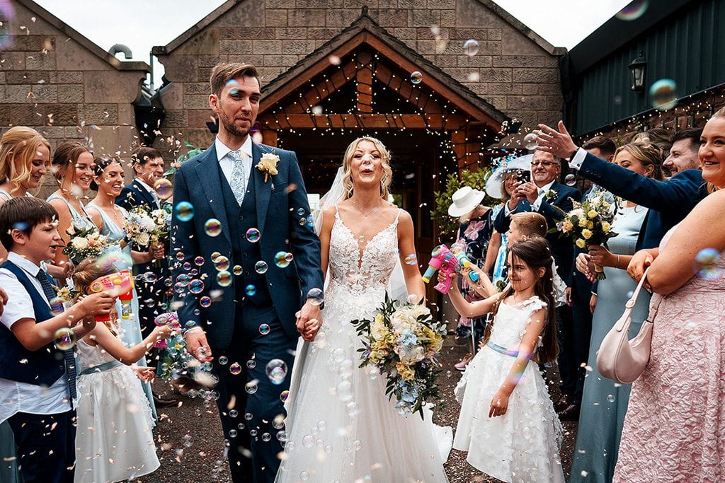 Nicola and Callam surrounded by guests, confetti and bubbles.